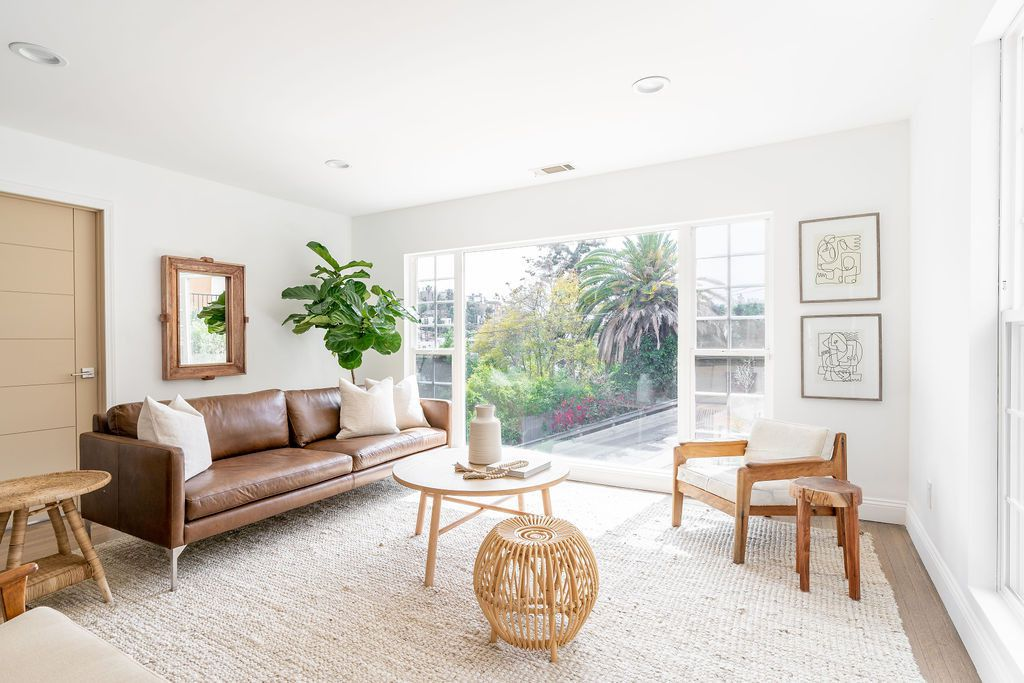 Stylish living room with leather sofa, wooden furniture, large windows, and indoor plant for cozy and inviting home decor.